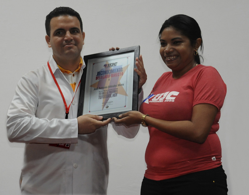 Rosa María Ramírez Montero, integrante del Buró Nacional de la UJC, entrega el reconocimiento al joven galeno. delegado ujc lenin 2