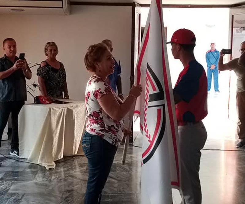 Bárbara Díaz, miembro del Buró Provincial de Partido entregó la Bandera al pitcher Campeón Olímpico Danny Betancourt. Fotos tomadas del perfil de Facebook de Roberto Carlos Rodríguez cafetaleros bandera liga élite 2
